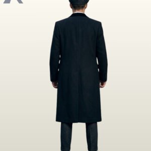 Full rear view of a male model wearing a long black wool Peaky Blinders style overcoat with a velvet collar insert and tweed flat cap.