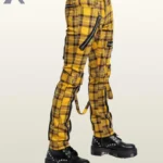 Three-quarter side profile view of a model wearing yellow tartan plaid punk bondage pants displaying thigh buckled straps and silver zipper pockets.