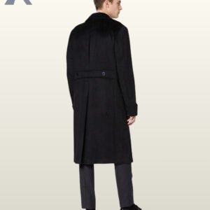 Full rear view of a model wearing a long black wool officer coat highlighting a buttoned rear half-belt waist, center pleat, and long back split vent.