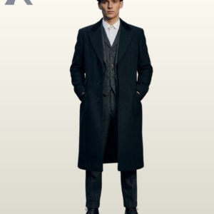 Full front view of a model wearing an open black wool single-breasted overcoat over a grey tweed three-piece suit, pocket watch chain, and newsboy cap.