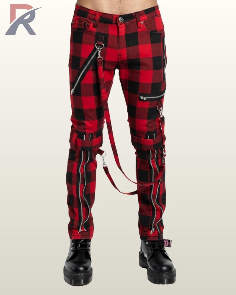 Full front view of a male model wearing crimson red and black buffalo plaid punk bondage pants with silver metal zippers, thigh buckles, and hanging D-ring bondage straps.