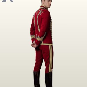 Side profile view of a model wearing a red military hussar uniform suit showing gold sleeve embroidery, cuff detailing, and dual gold trouser stripes.