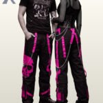 Gothic couple posing in wide-leg black cargo pants featuring high-contrast pink skull artwork.