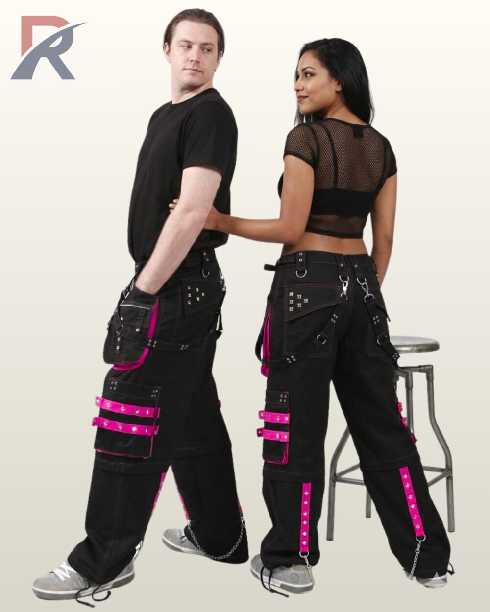 Side and back view of a couple wearing black gothic cargo pants accented with vivid hot pink studded straps, pockets, and hanging chains.