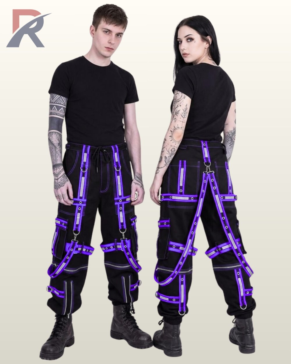 Couple in black gothic reflective cargo trousers trimmed with purple eyelet straps, suspender harnesses, and cargo pockets.