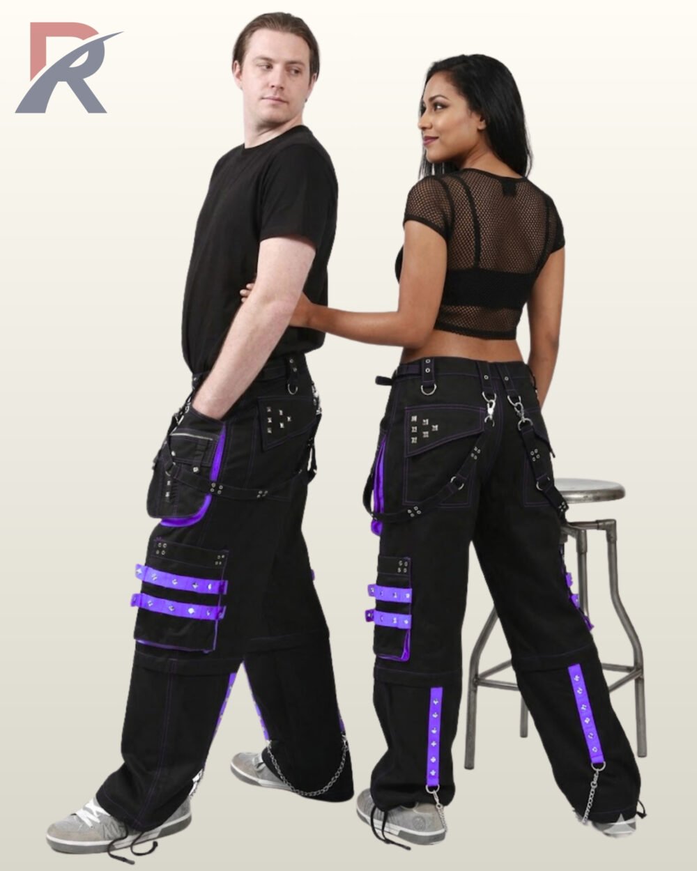 Rear angle of a man and woman modeling cyber goth wide-leg trousers featuring purple trim, grommets, and silver chains.