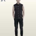 Full front model view of a men's black sleeveless gothic shirt with hands in pockets, featuring metallic chest studs, shoulder rivets, and a flap chest pocket.