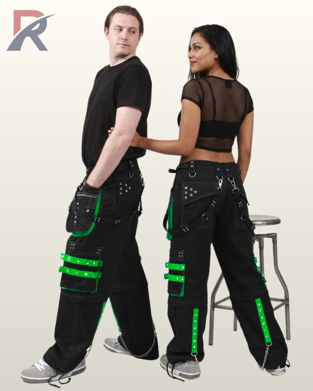 Side and rear view of a couple wearing black gothic wide-leg cargo trousers trimmed with bright neon green studded straps and metal chains.