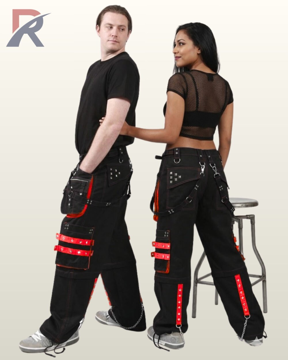 Side and back view of a couple wearing black gothic cargo pants trimmed with red studded straps, detachable pockets, and metal chains.