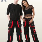 Front view of a man and woman wearing black gothic cargo pants accented with bright red trim, metal studs, and hanging chain hardware.