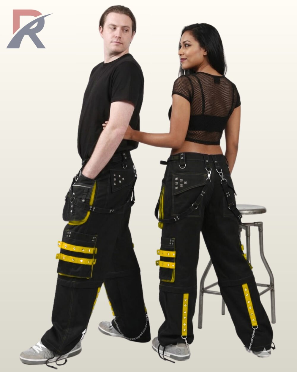 Side and back view of a couple wearing black gothic wide-leg cargo pants featuring bright yellow studded straps and hanging metal chains.