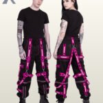 Man and woman modeling dark techwear joggers highlighting vibrant hot pink reflective tape and metal hardware.