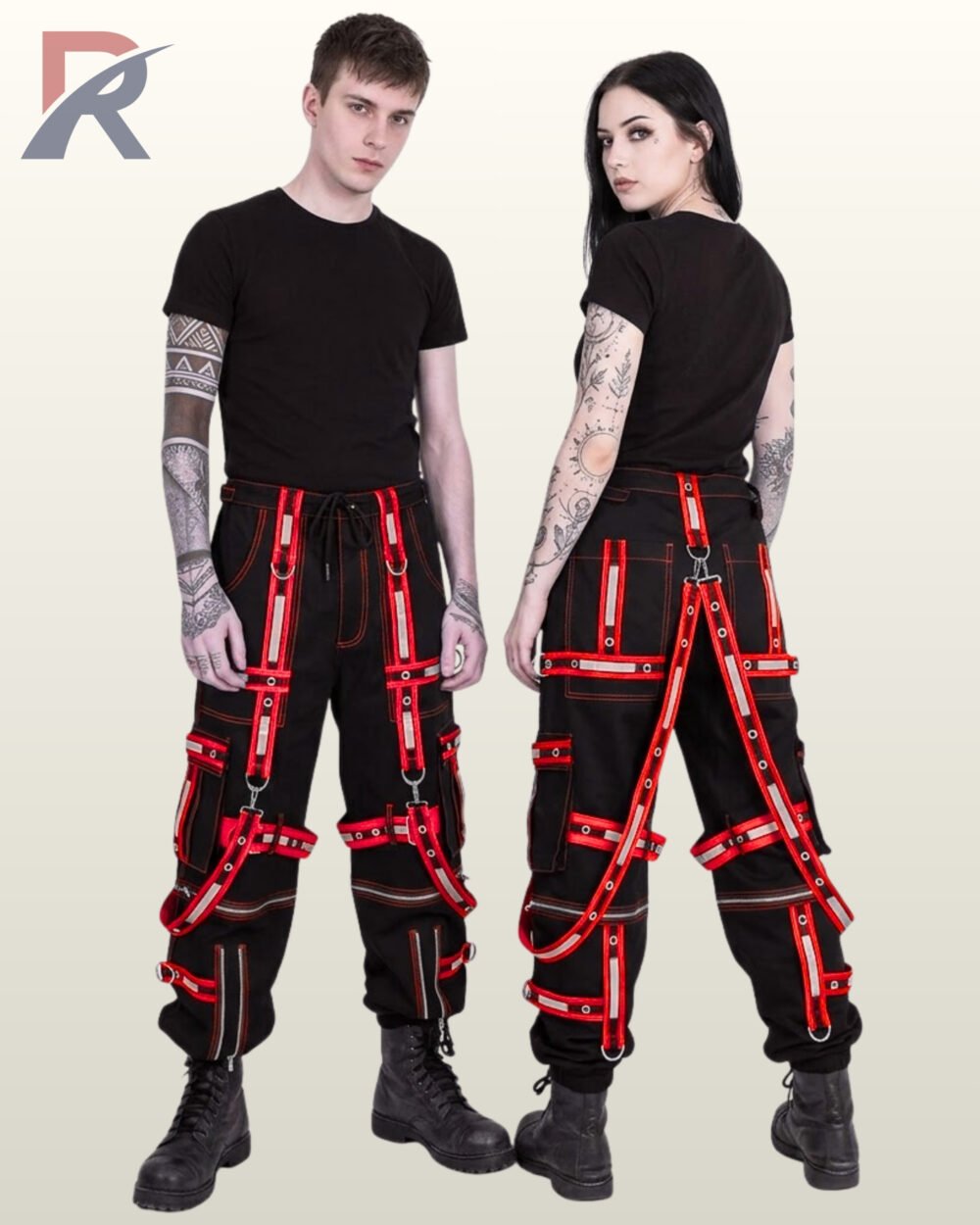 Couple wearing black gothic reflective cargo trousers featuring bold red eyelet straps, suspender harness details, and metal rings.