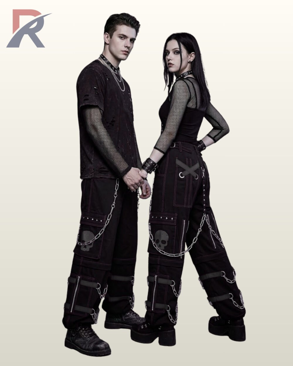 Couples model shot of all-black gothic cyberpunk cargo trousers displaying subtle grey skull pocket graphics, black buckle leg straps, and silver chains.