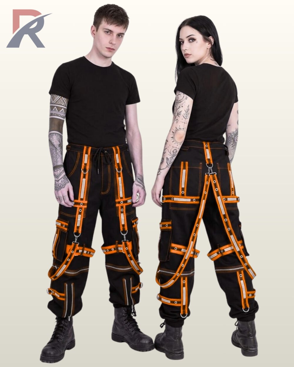 Couple in black gothic cargo pants styled with bright orange reflective straps, grommeted trim, and suspender harnesses.