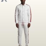 A Black man wearing a premium white streetwear tracksuit featuring a button-up jacket and matching sweatpants with a side maroon stripe.