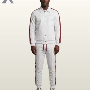 A Black man wearing a premium white streetwear tracksuit featuring a button-up jacket and matching sweatpants with a side maroon stripe.