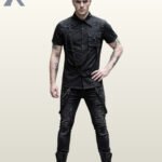 Full front model view of a men's black gothic industrial short-sleeve shirt featuring metal studs, shoulder D-rings, chest pocket, and hanging harness straps.