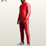 A full-length view of a man modeling a vibrant red leather tracksuit with classic white athletic stripes.