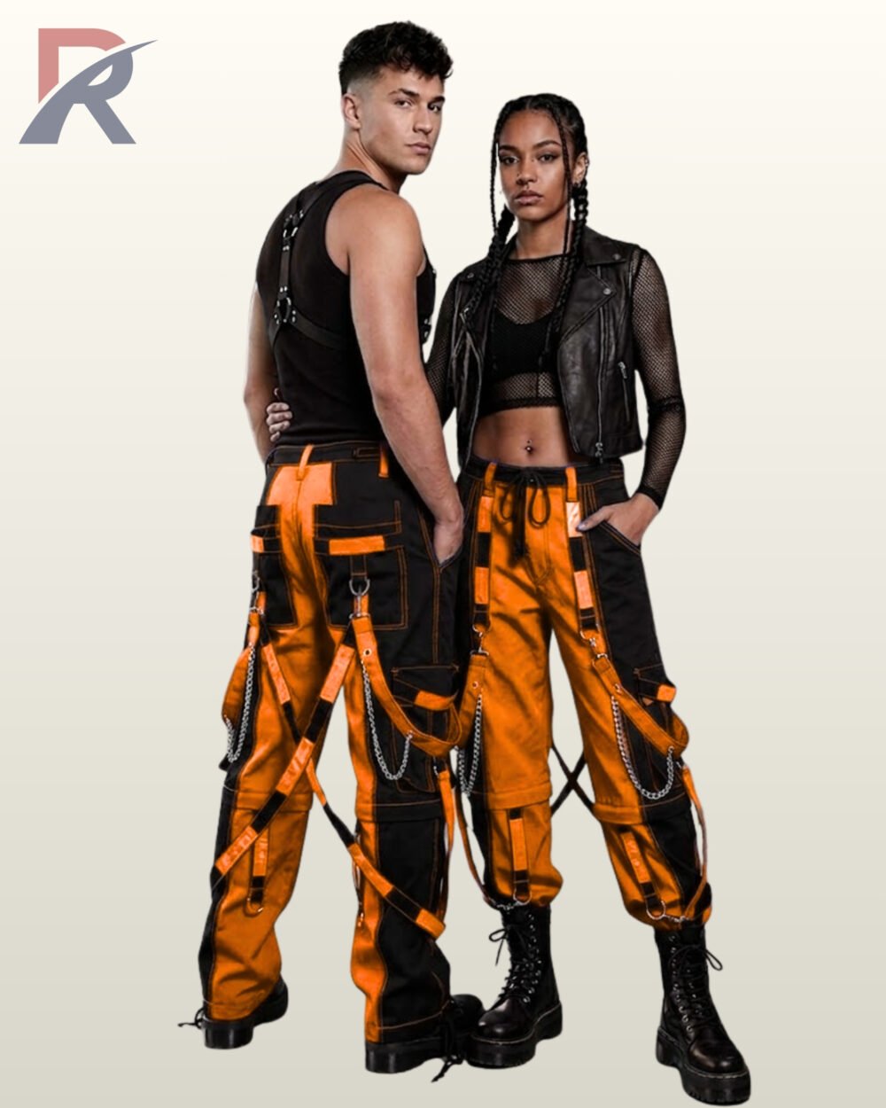 Couples model view of two-tone orange and black cyberpunk cargo trousers displaying D-ring bondage straps, side metal chains, and platform boots.