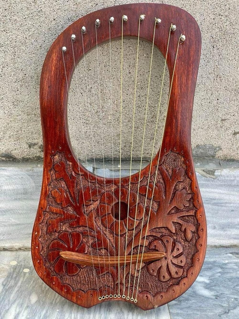 Carved 10-string wooden lyre harp with a rich reddish stain, displaying brass string eyelets, curved bridge, and floral relief carvings.