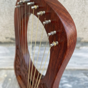 Angled close-up shot of the top arm of a rosewood lyre harp highlighting ten metal tuning pins wrapped with steel strings.