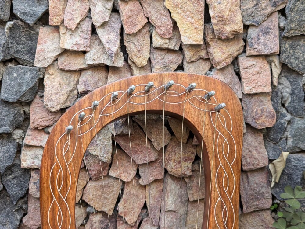 Detailed shot of silver tuning pins and steel strings attached to the curved wooden frame of a 10-string lyre harp.