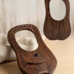 Front view of a 10-string dark rosewood lyre harp resting on a wooden table with hand-carved Celtic braid border, sound hole knotwork, and a rear view inset.