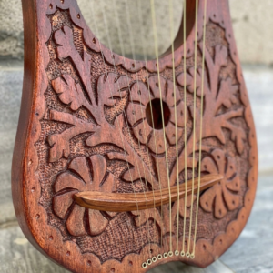 Close-up view of the soundboard of a 10-string rosewood lyre harp featuring hand-carved floral motifs, textured background, and a curved wooden bridge.