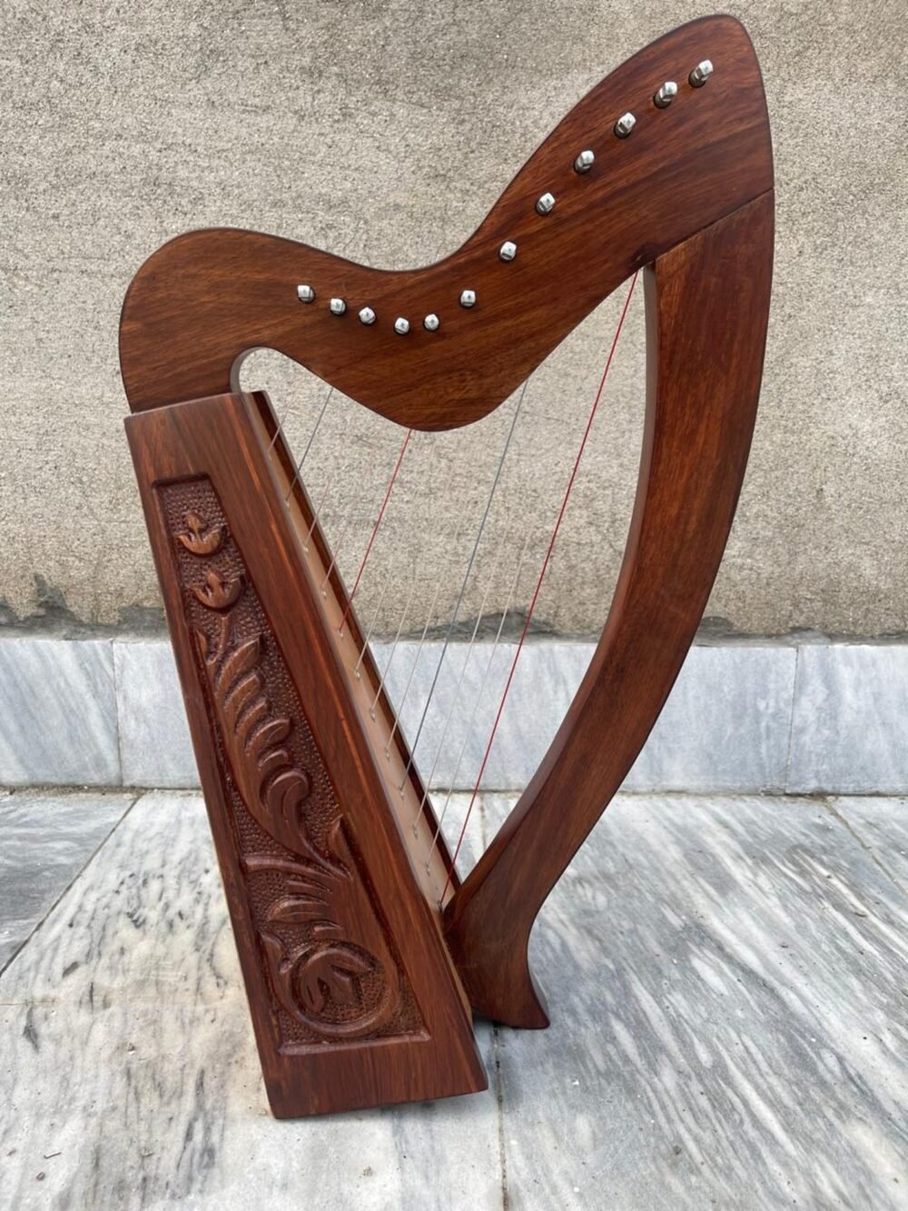 Close-up view of a 12-string hand-carved rosewood Irish Celtic lap harp highlighting hand-carved floral soundboard engravings and silver tuning pins.