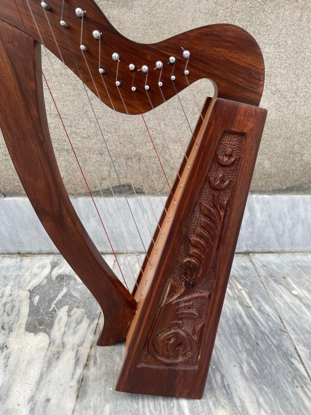 Handmade rosewood leverless Celtic folk harp featuring intricate floral wood carvings, curved pillar, and multicolored strings.