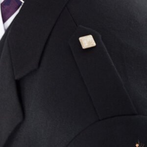 Close-up view of a men's black Argyle kilt jacket shoulder featuring a flat cloth epaulet fastened with a square silver button.