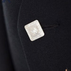 Detailed view of a traditional Scottish silver square button with ornate design on a black Argyle kilt jacket.
