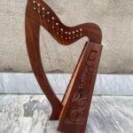 Full view of a 12-string handcrafted rosewood Irish Celtic lap harp with hand-carved floral side panels and silver tuning pins resting on a marble floor.