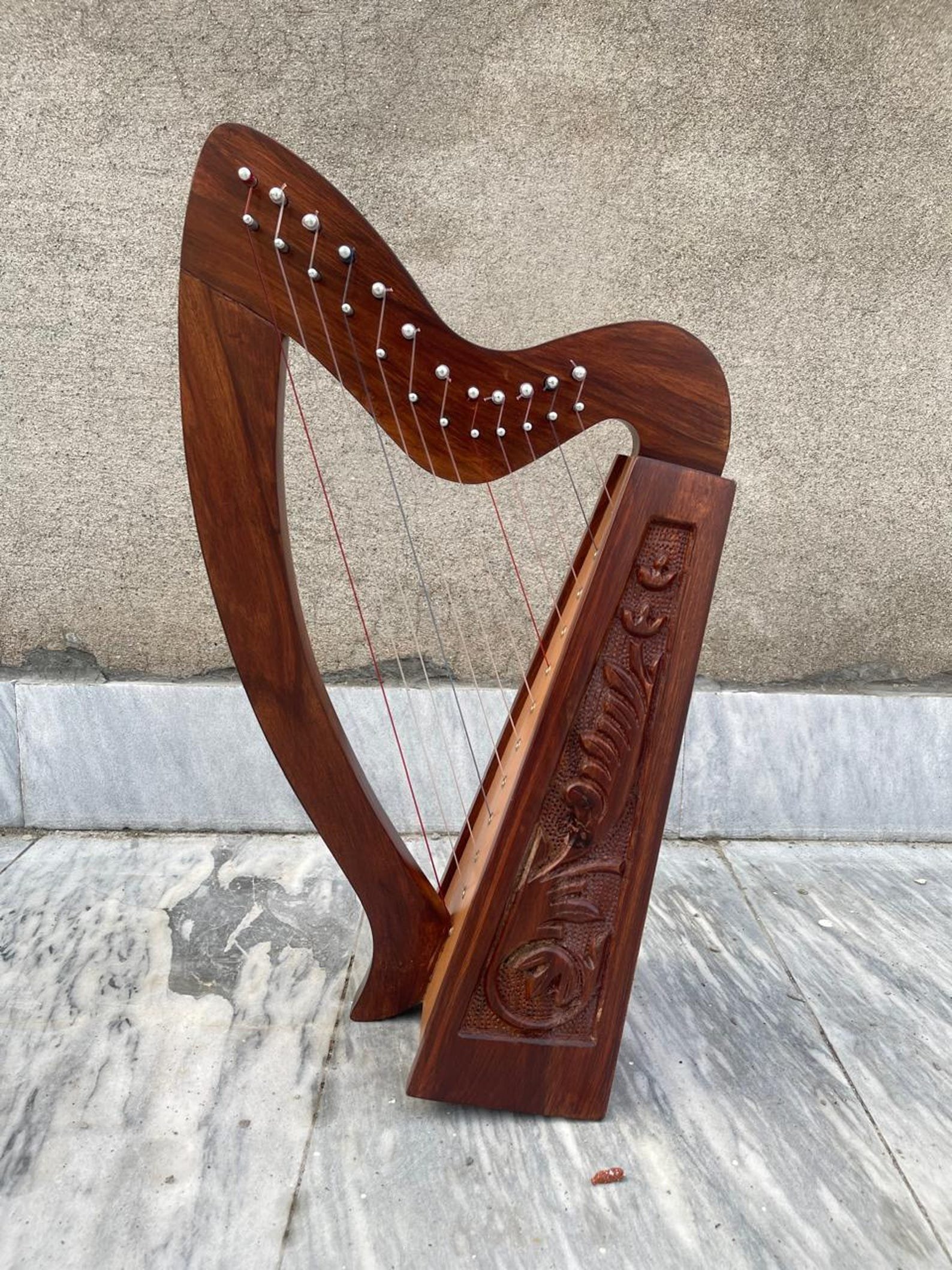 Full view of a 12-string handcrafted rosewood Irish Celtic lap harp with hand-carved floral side panels and silver tuning pins resting on a marble floor.