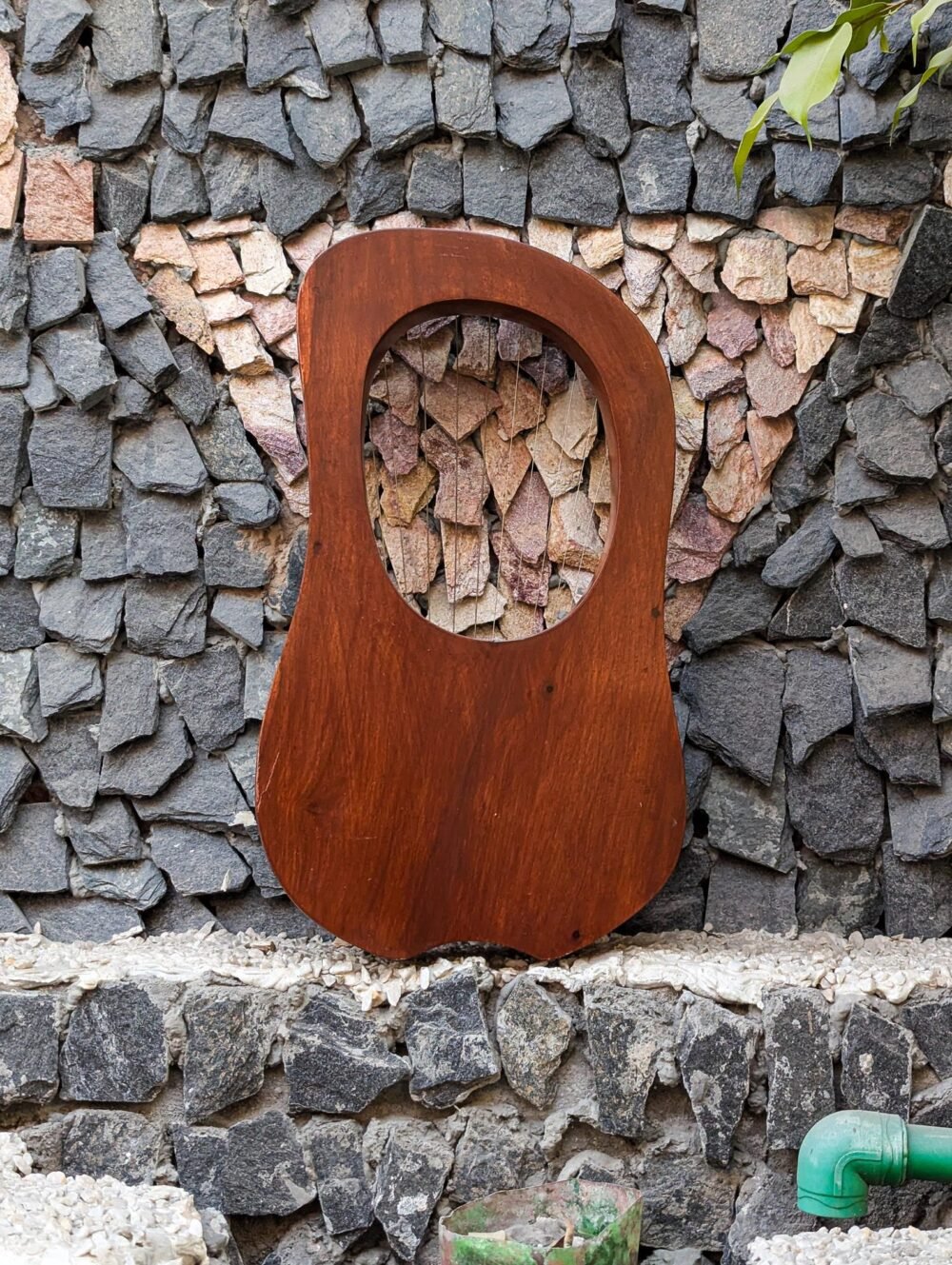 Full rear view of a 10-string handcrafted solid rosewood lyre harp resting against a stone wall, showcasing natural reddish-brown wood grain.