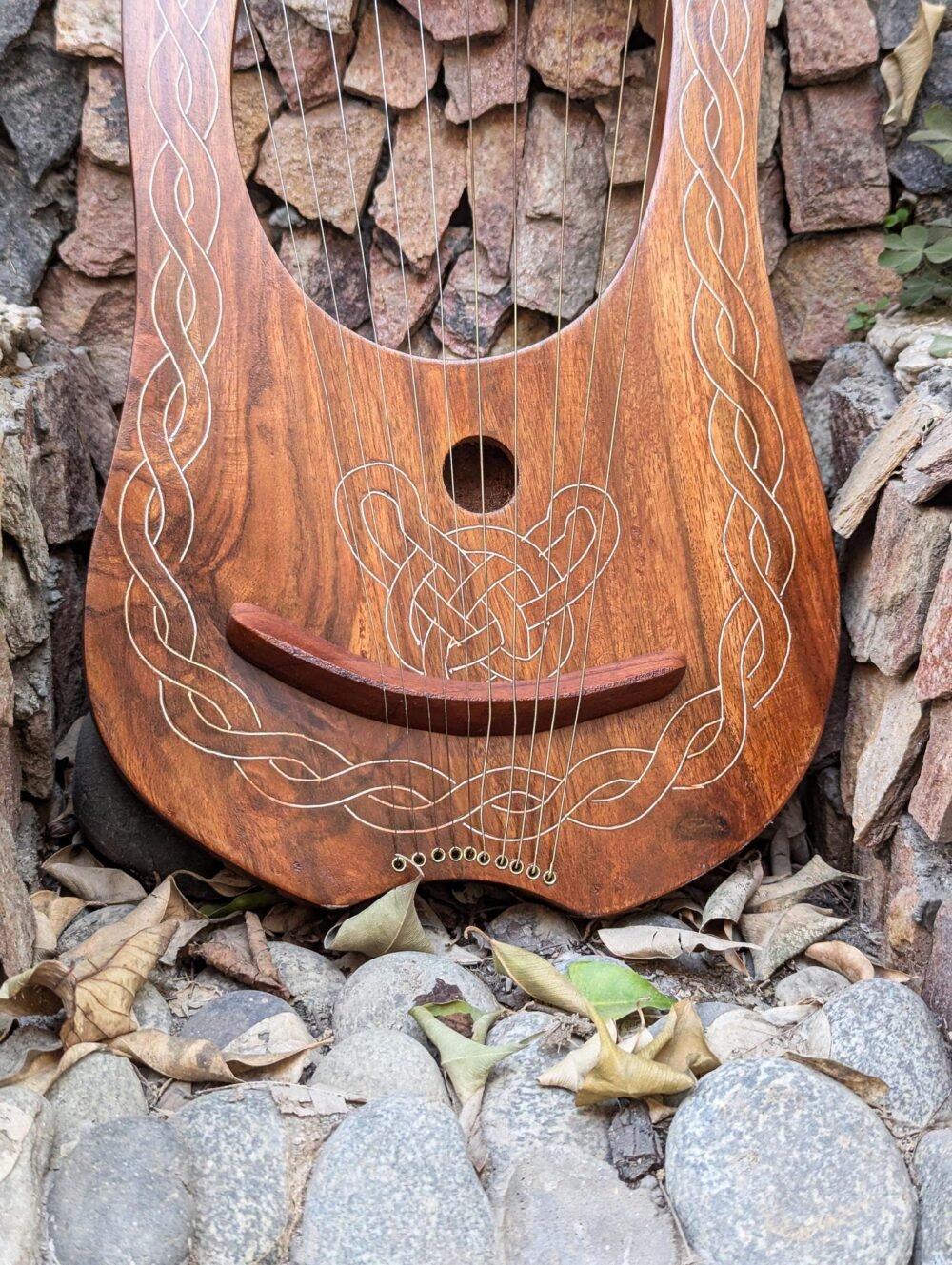 Close-up view of the soundboard of a wooden lyre harp featuring a circular soundhole, wooden bridge, string eyelets, and engraved Celtic knotwork.