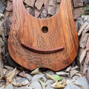 Close-up view of the soundboard of a wooden lyre harp featuring a circular soundhole, wooden bridge, string eyelets, and engraved Celtic knotwork.